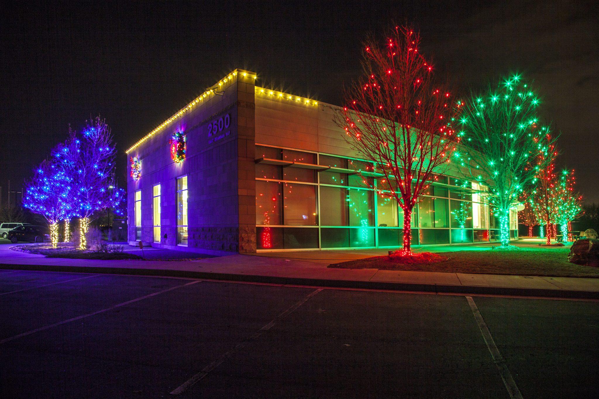 Commercial building with warm white roofline lights and color-wrapped trees