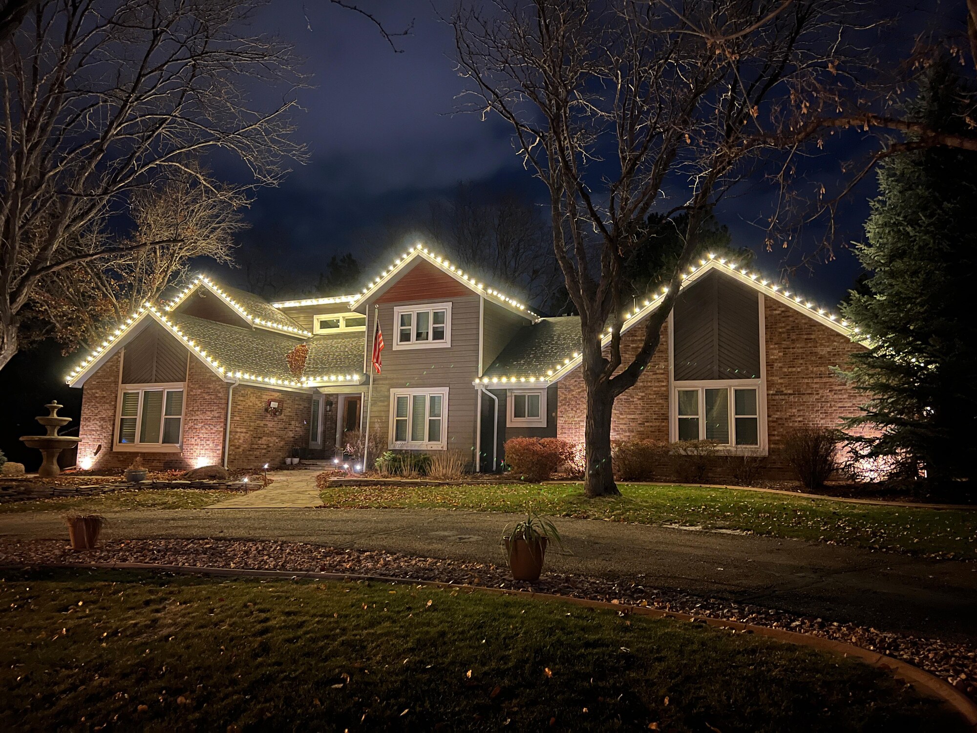 Multi-gable home with warm white roofline lights and brick uplighting