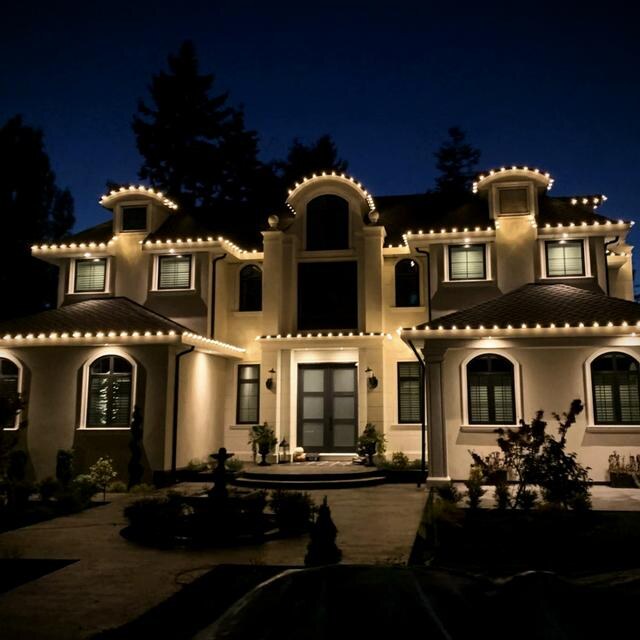 Luxury home with warm white roofline lights and arched entry