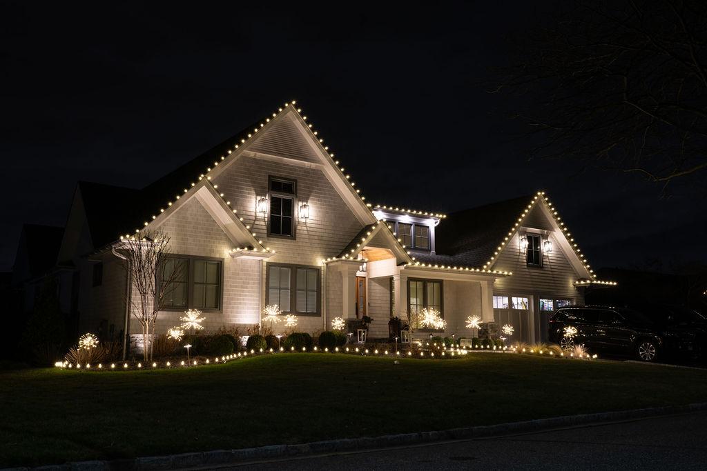 Luxury home with warm white roofline lights and starburst landscape accents