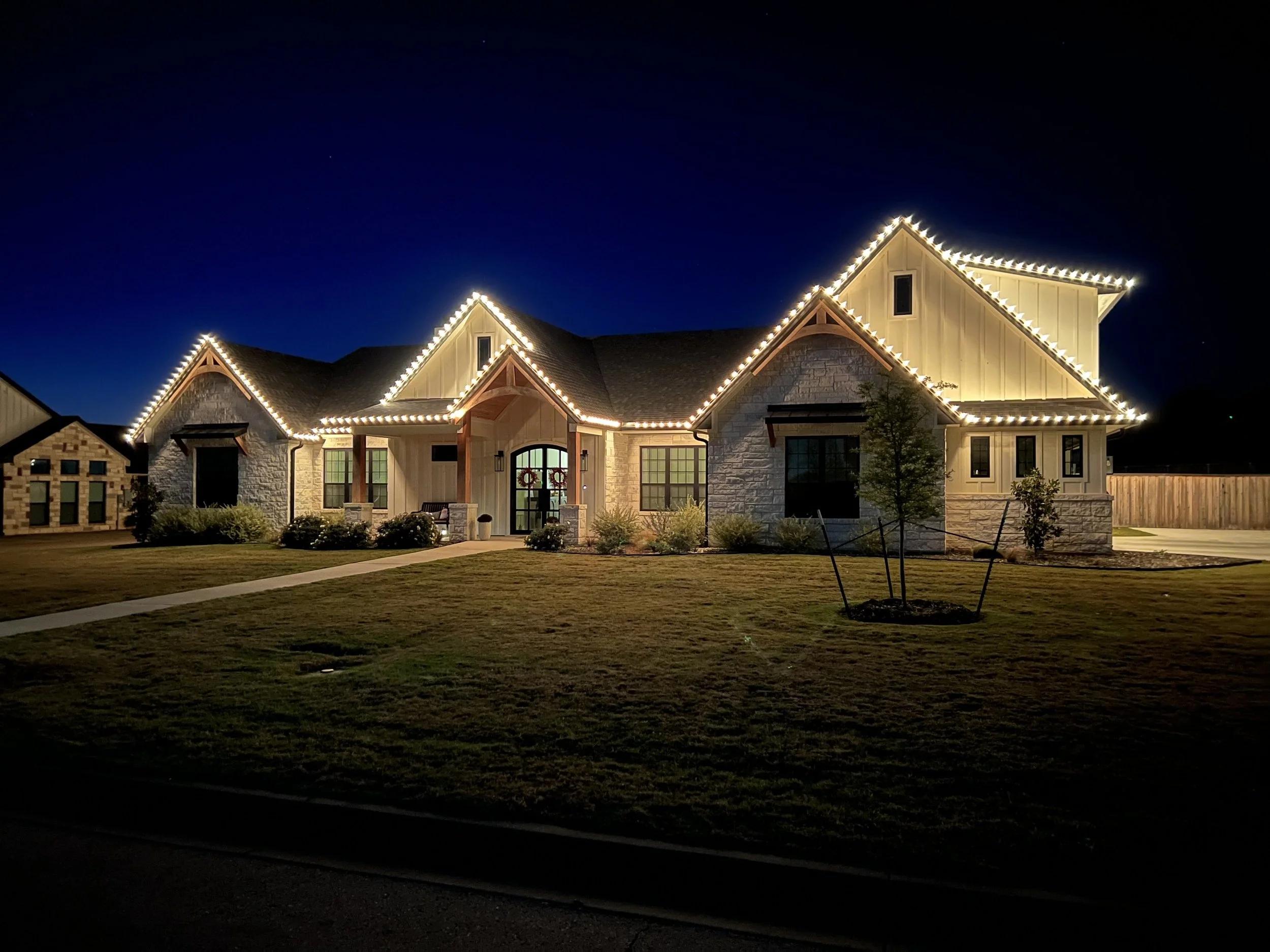 White farmhouse with warm white roofline Christmas lights
