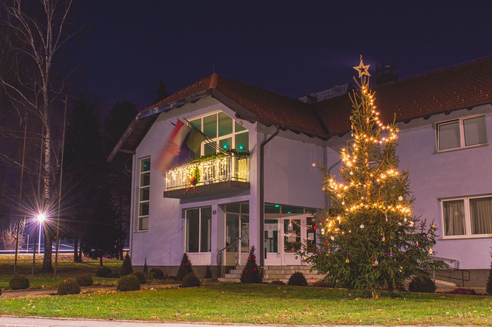 Building decorated with warm white Christmas lights and an illuminated outdoor Christmas tree at night.